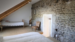 Een slaapkamer met een schuine kap, een stenen muur, een bed, een stoel en een kleine tafel.