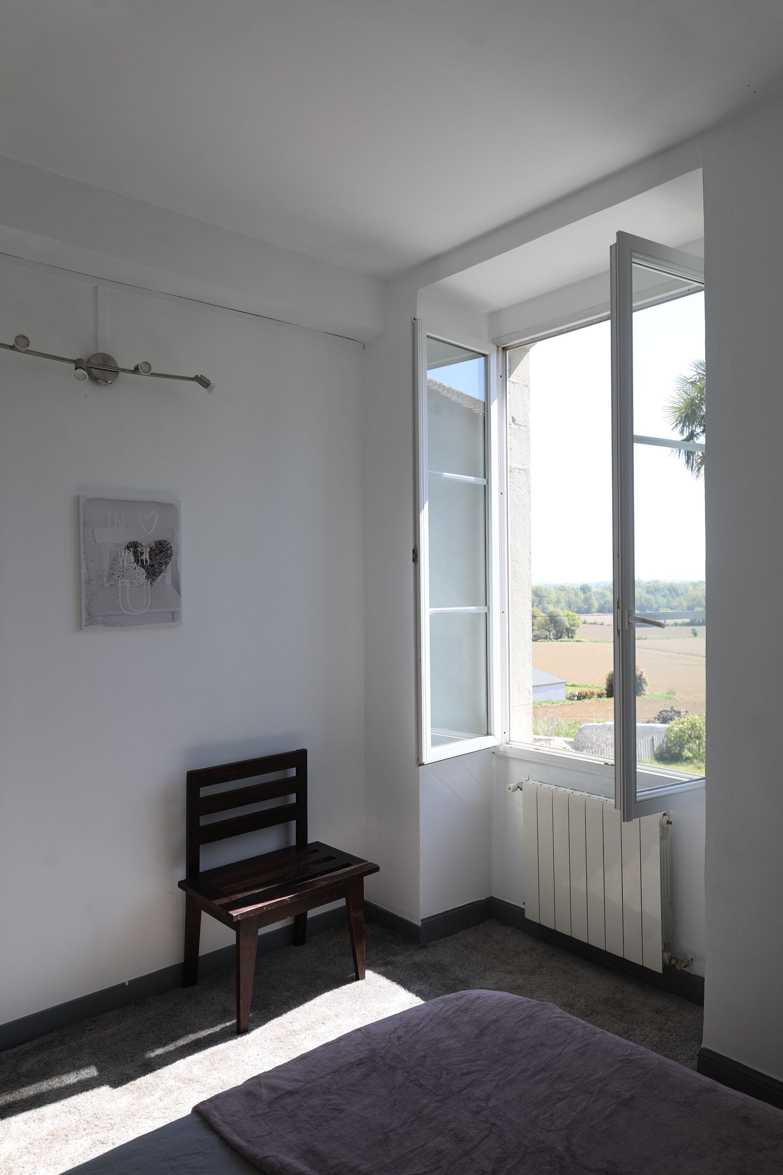 Una habitación con una silla de madera, un radiador y una ventana con contraventanas abiertas.