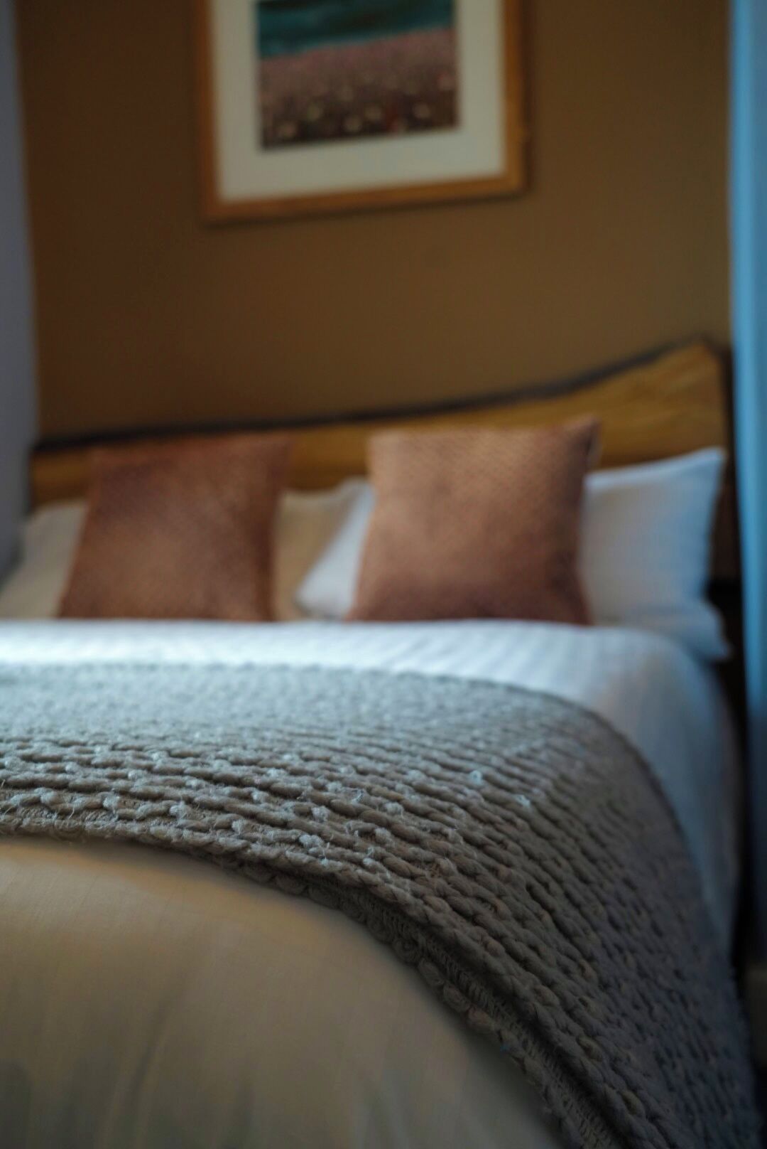A bed with a knitted blanket, a wooden headboard, and two pillows.
