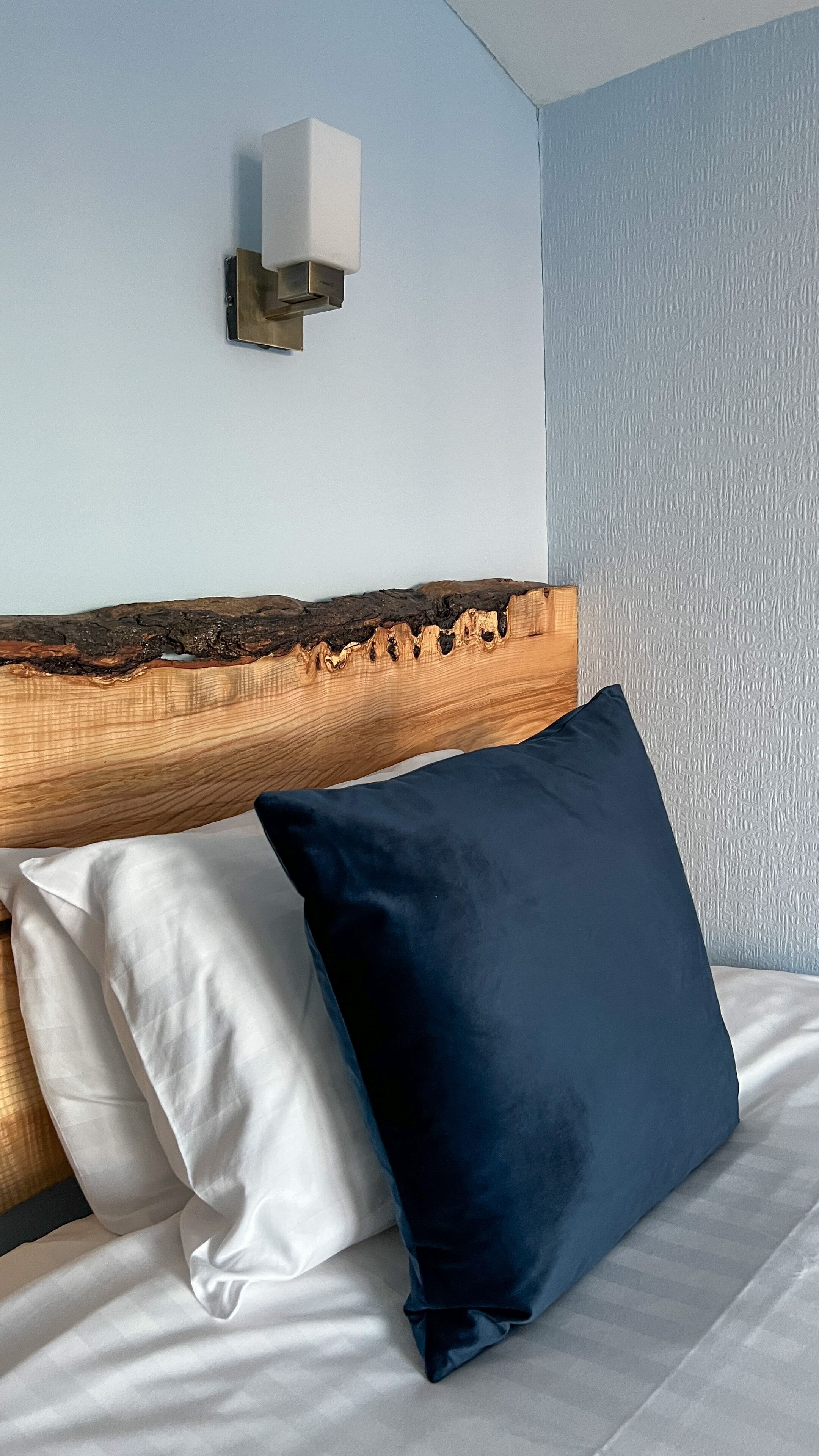 A bed with a wooden headboard, two pillows, and a wall-mounted light fixture.