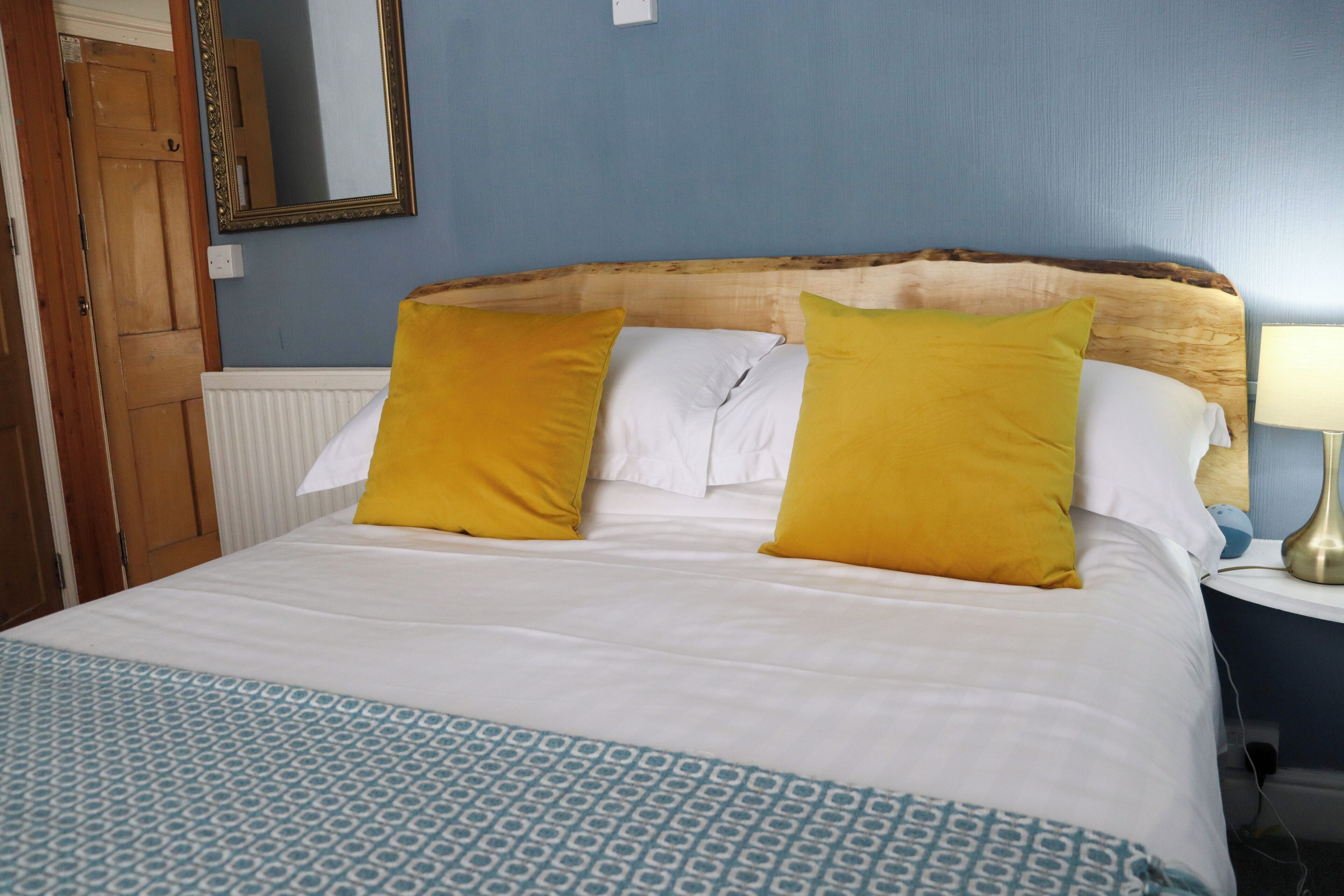A bed with white and yellow pillows, a patterned blue and white bedspread, and a wooden headboard.