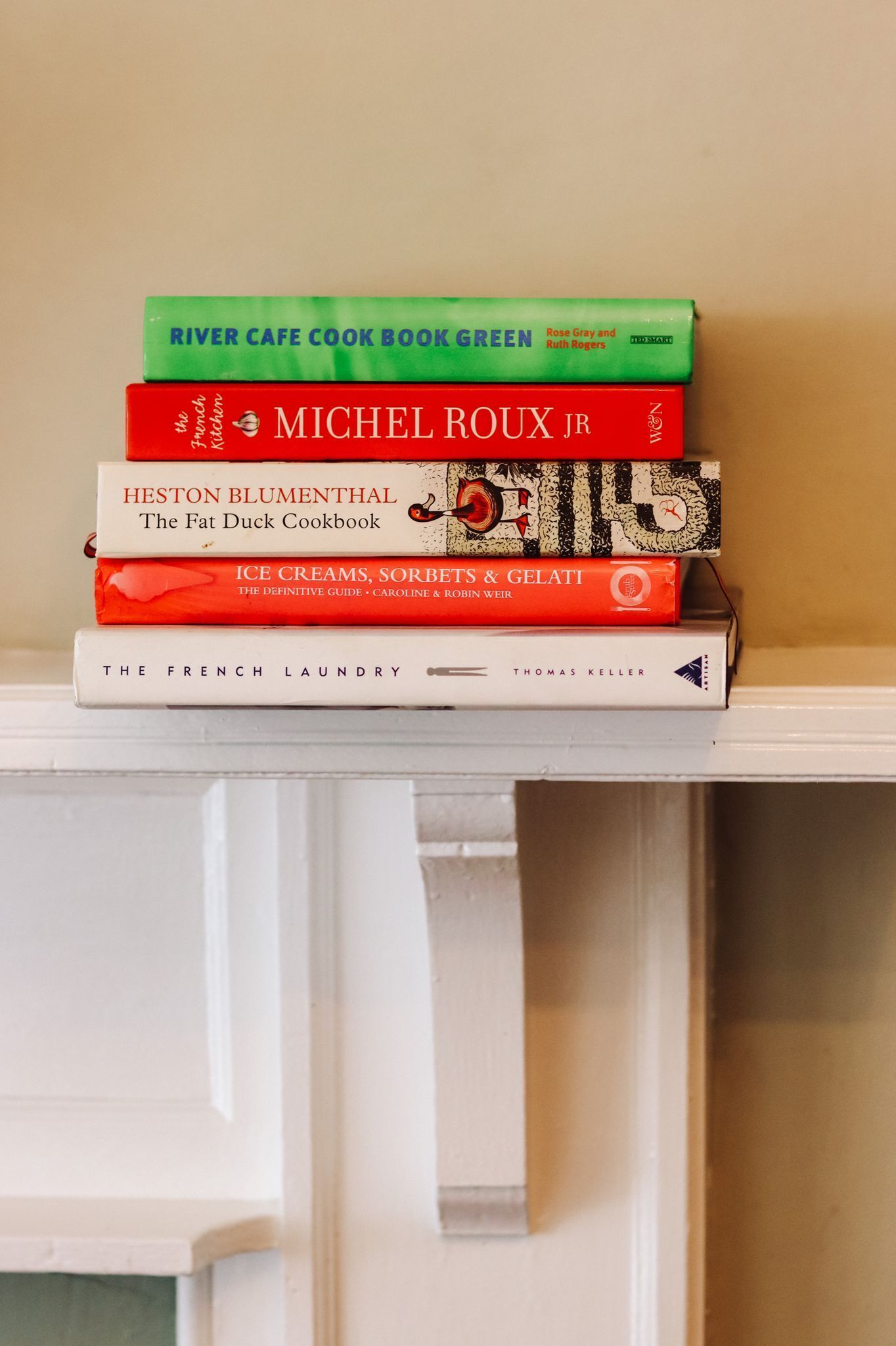 A stack of cookbooks on a white shelf.