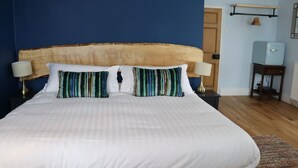 Uma cama com roupa de cama branca e almofadas listradas, uma cabeceira de madeira e uma mesa de cabeceira com abajur.