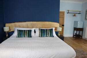 Una cama con ropa de cama blanca y almohadas a rayas, un cabecero de madera y una mesita de noche con una lámpara.