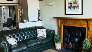 Uma sala de estar com um sofá de couro verde, uma lareira e um quadro pendurado na parede.
