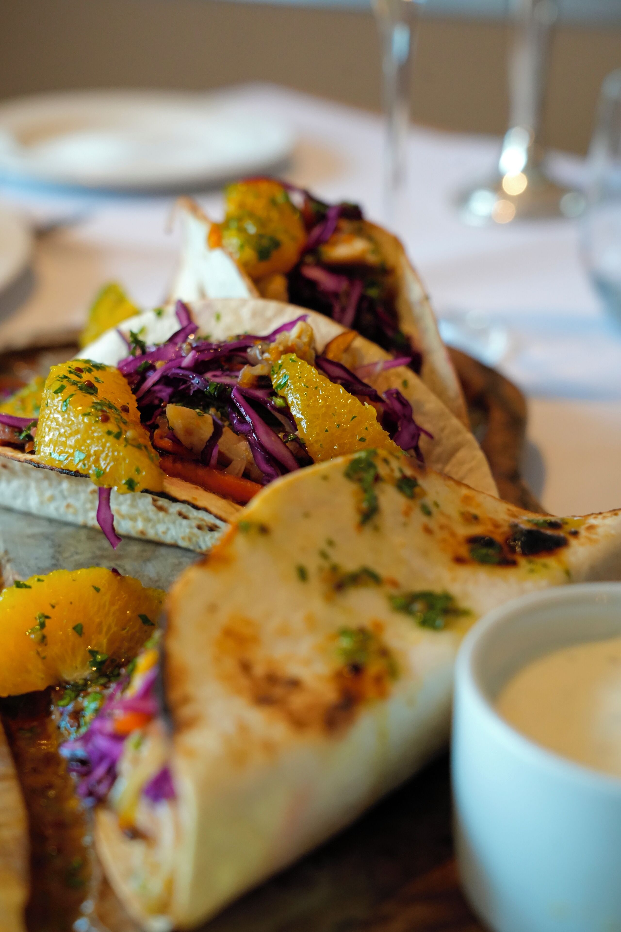 A plate of tacos with grilled meat, vegetables, and a side of sauce.