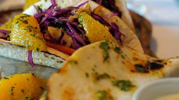 A plate of tacos with grilled meat, vegetables, and a side of sauce.