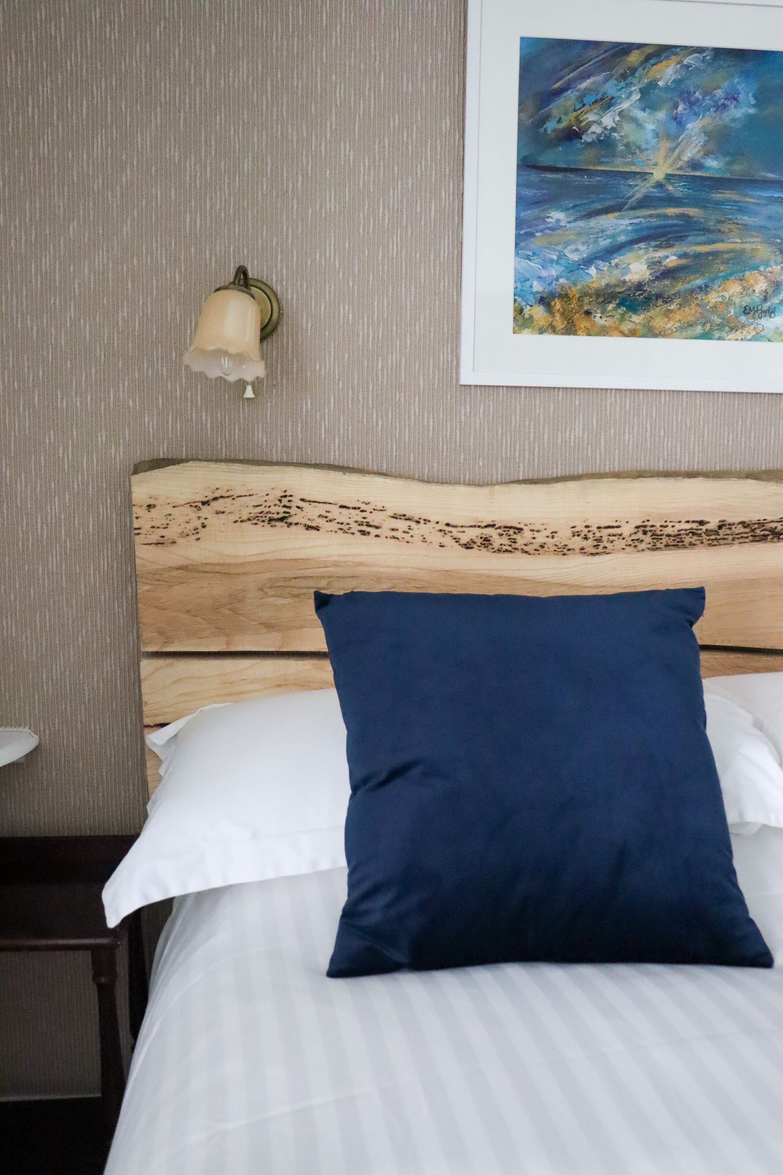 Een net opgemaakt bed met een houten hoofdbord, een wit kussen en een blauw kussen.