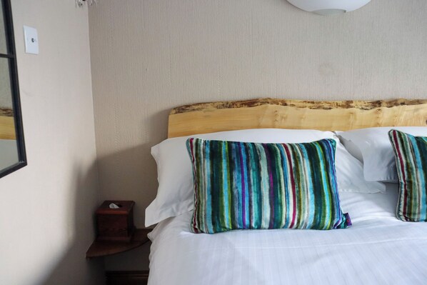 Habitación de hotel con cabecera de madera, ropa de cama blanca y almohadas a rayas.