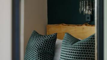 Quarto com cama, almofadas estampadas em verde, cabeceira de madeira e luminária suspensa.