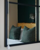 Un dormitorio con una cama, almohadones estampados verdes, un cabecero de madera y una lámpara colgante.