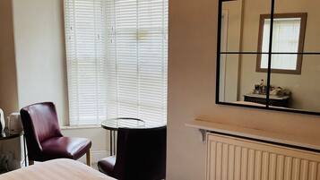 Habitación de hotel con cama, una silla, una mesita, un radiador y ventana con persianas.