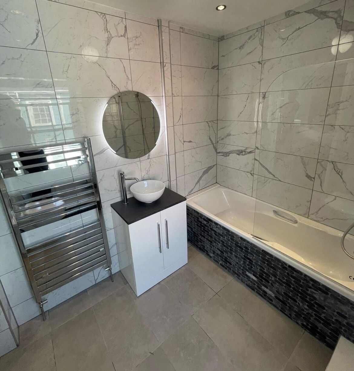 Une salle de bain moderne avec un pare-baignoire en marbre, une baignoire sur pieds et un meuble-lavabo intégré doté d’un évier et d’un miroir.