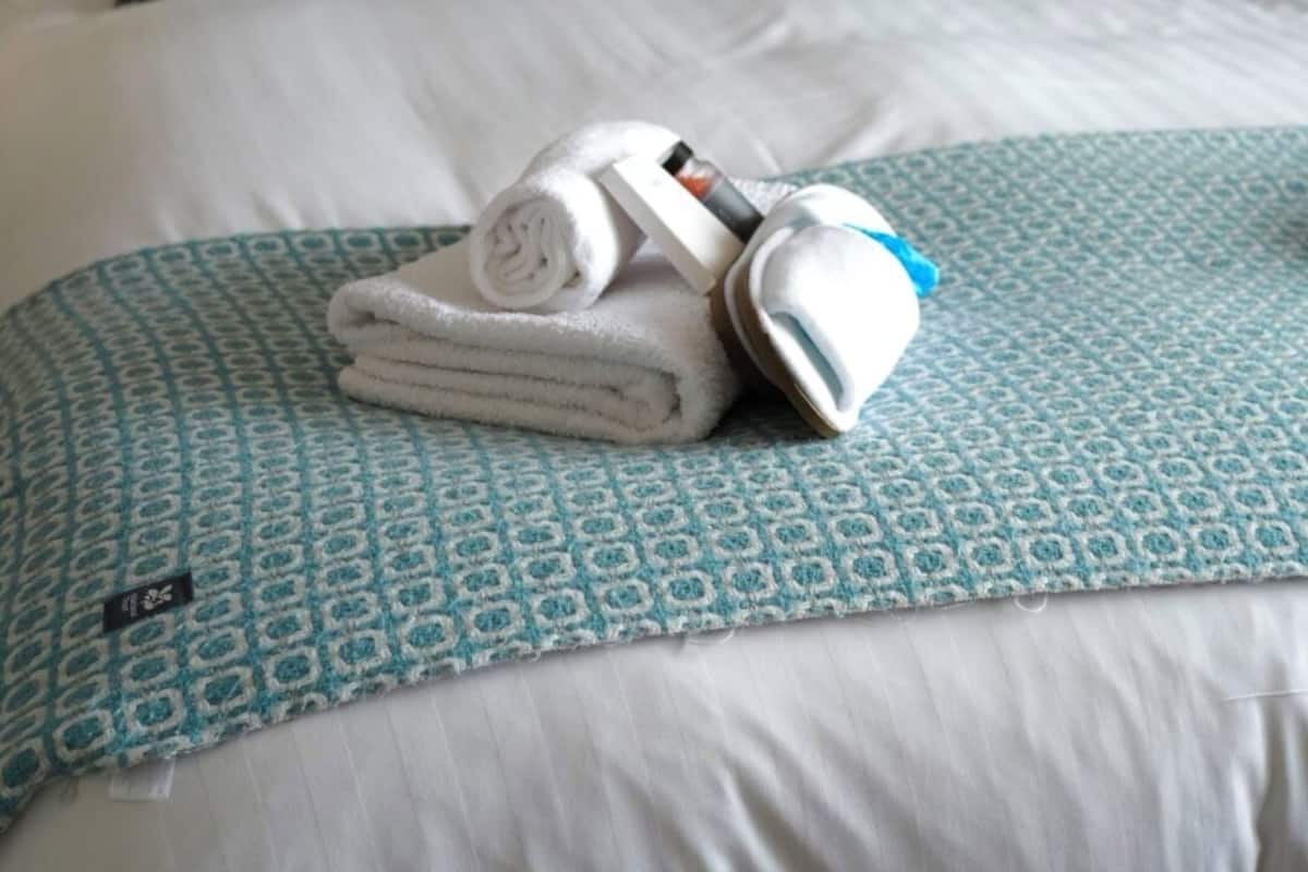Un lit bien fait, avec une couvre-lit à motifs, des oreillers et une serviette pliée sur laquelle est posé un appareil.