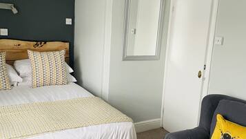 Um quarto com uma cama, uma cadeira, um espelho e uma porta.