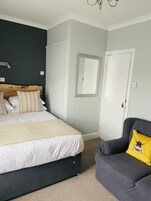 Um quarto com uma cama, uma cadeira, um espelho e uma porta.