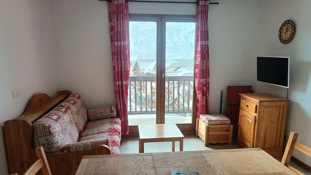 A room with a wooden sofa, a dining table with chairs, a small cabinet, and a TV on the wall. - 6 people + baby Valmeinier 1800 runs and 150 meters ESF (Valmeinier)