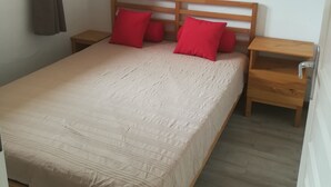 A bedroom with a wooden bed frame, a beige bedspread, and two nightstands with red pillows. - 6 people + baby Valmeinier 1800 runs and 150 meters ESF (Valmeinier)