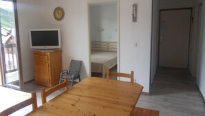 A dining area with a wooden table and chairs, a television on a wooden cabinet, and a mirror on the wall. - 6 people + baby Valmeinier 1800 runs and 150 meters ESF (Valmeinier)