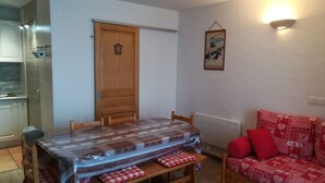 A dining area with a wooden table and benches, a red sofa, and a kitchen in the background. - 6 people + baby Valmeinier 1800 runs and 150 meters ESF (Valmeinier)
