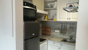 A compact kitchen with a stainless steel refrigerator, a microwave, a dishwasher, and a sink. There are white cabinets, a wooden rack, and a hanging utensil rack. - 6 people + baby Valmeinier 1800 runs and 150 meters ESF (Valmeinier)
