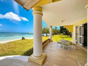 Eine überdachte Terrasse mit Blick auf Strand und Meer, ausgestattet mit weißen Säulen und einem Fliesenboden.