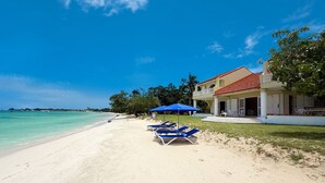 Une plage de sable blanc, un ciel bleu azur et un bâtiment avec un toit rouge.