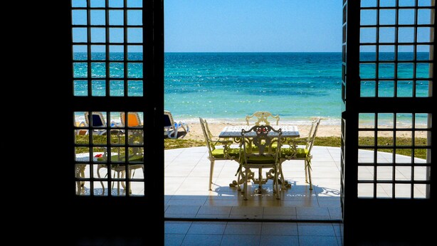 Une porte ouverte donnant sur une plage, avec une table et des chaises à l’extérieur.