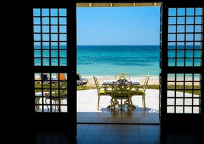 Eine offene Tür mit Blick auf einen Strand und einem Tisch mit Stühlen davor.