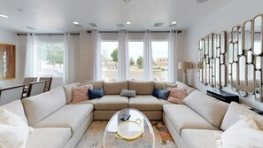 A modern living room with a sectional sofa, a glass coffee table, and a decorative mirror wall.