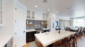 Una cocina moderna con armarios blancos, una isla central y una zona de comedor con sillas.