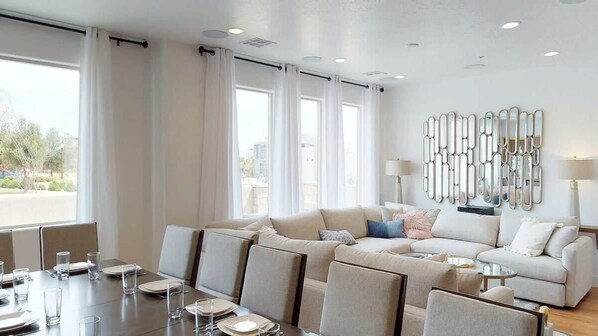 A modern hotel room with a large window, a sofa set, a dining table, and a decorative mirror wall.