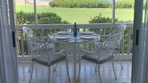 Un balcon avec une table en verre, dressée pour deux personnes, donnant sur une plage et l’océan.