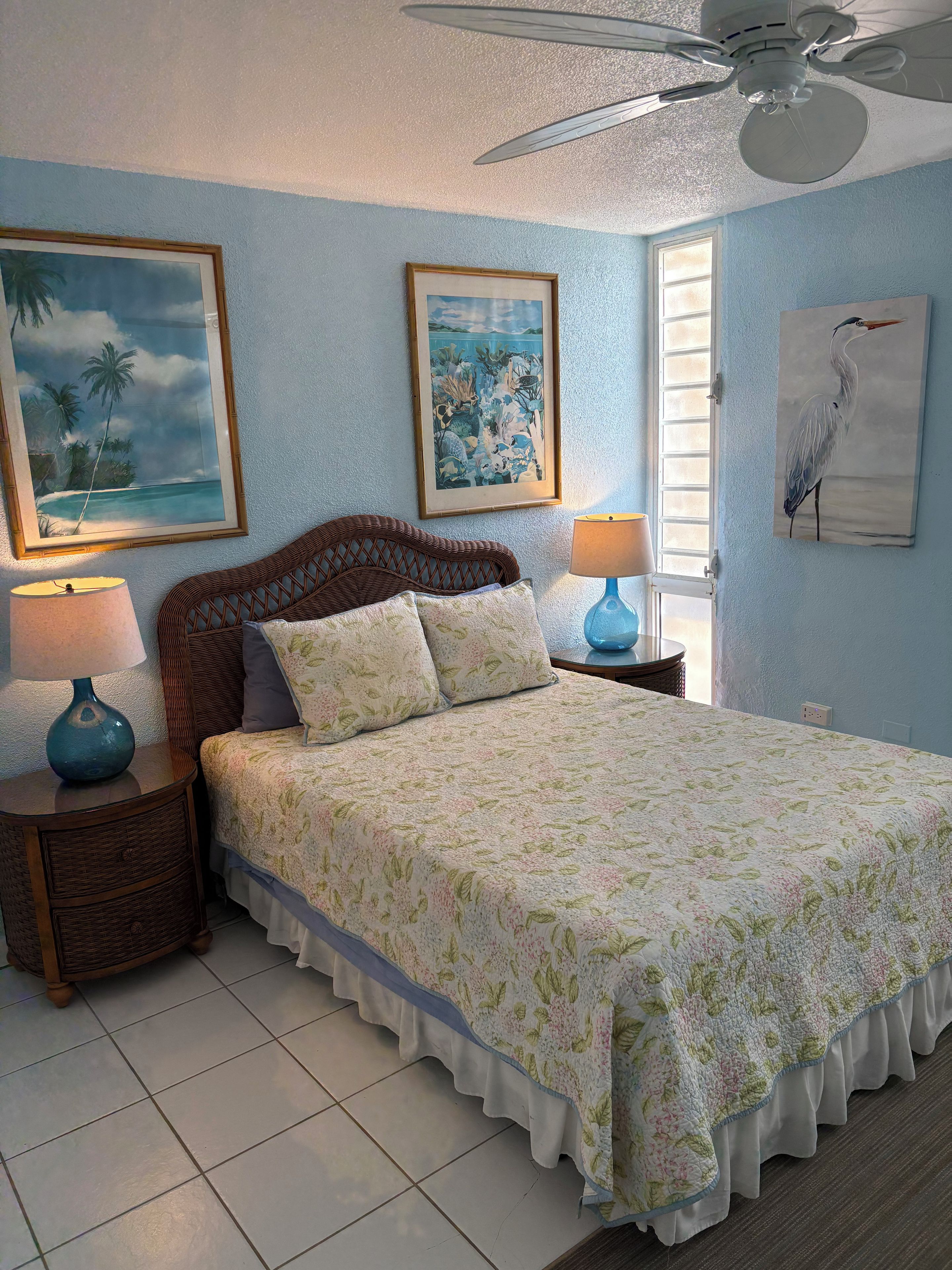 A bedroom with a bed, two nightstands, a ceiling fan, and wall art.
