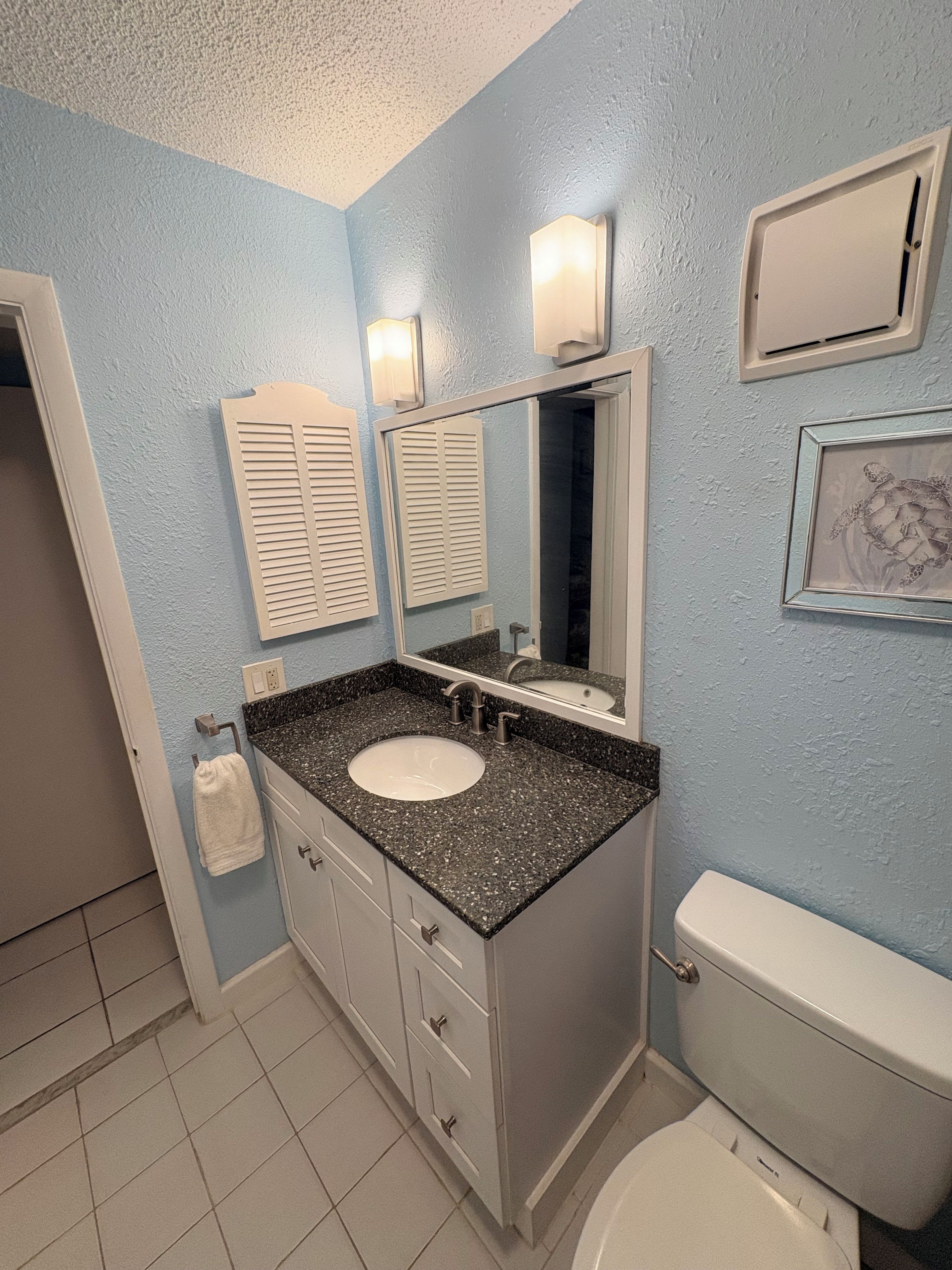A bathroom with a white toilet, a sink with a granite countertop, a mirror above the sink, and a towel rack.