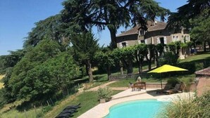 A swimming pool with a curved edge, surrounded by a patio area with lounge chairs and a yellow umbrella.