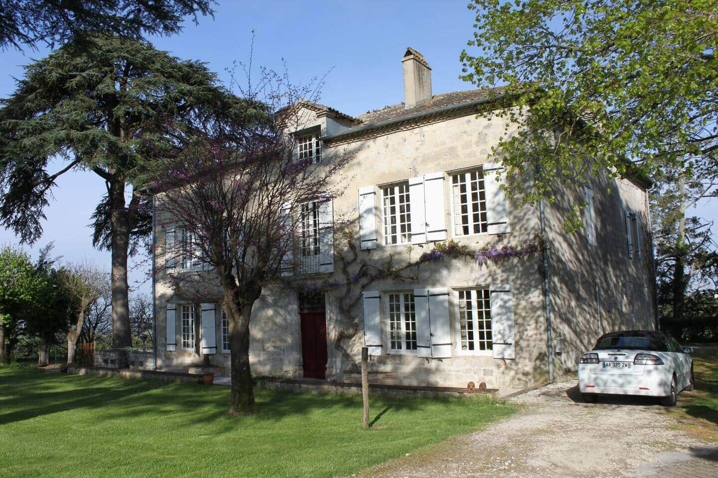 Un bâtiment en pierre de deux étages, avec une porte rouge, de nombreuses fenêtres et une voiture garée devant.