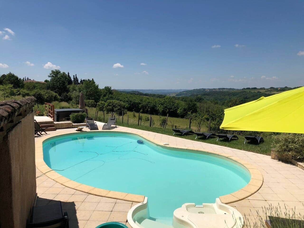 Ein Schwimmbecken mit gefliestem Deck, Liegestühlen und einem gelben Sonnensegel.