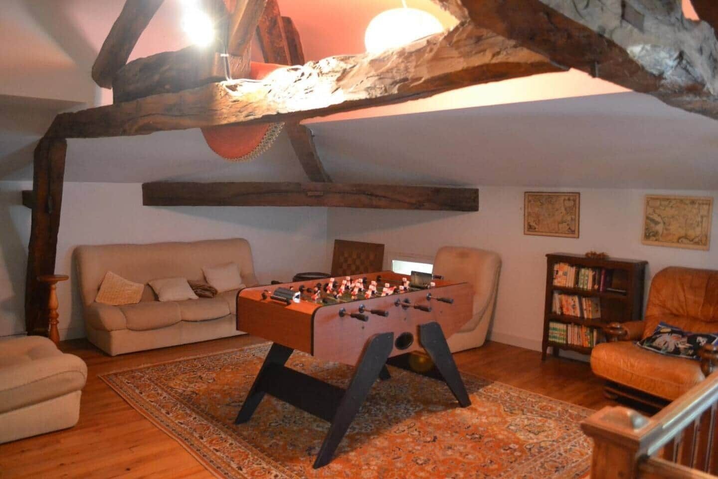 A cozy living room with a foosball table, a sofa, a bookshelf, and a rustic wooden ceiling.