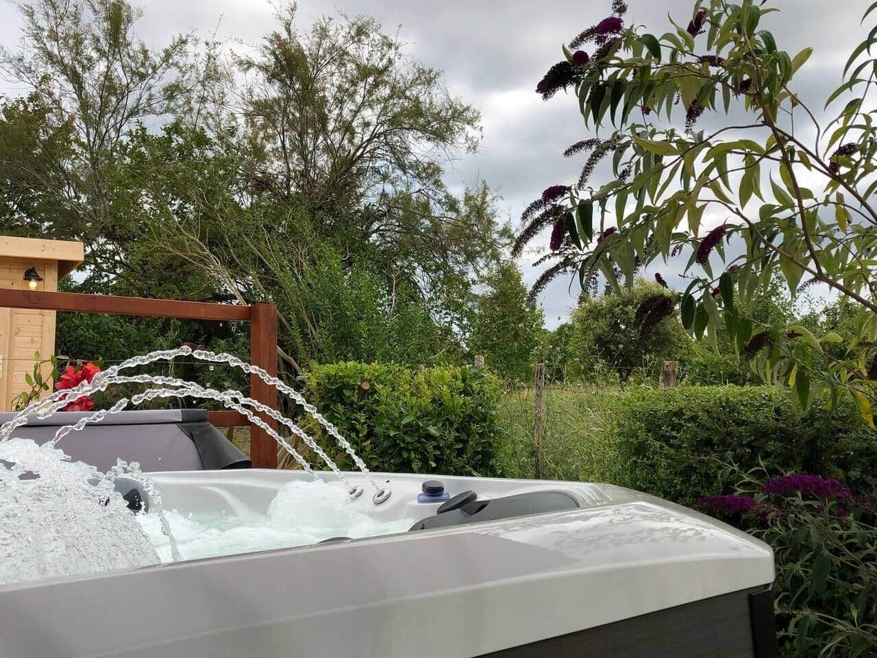 A hot tub with a wooden deck and a garden backdrop.