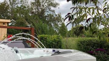 A hot tub with a wooden deck and a garden backdrop.