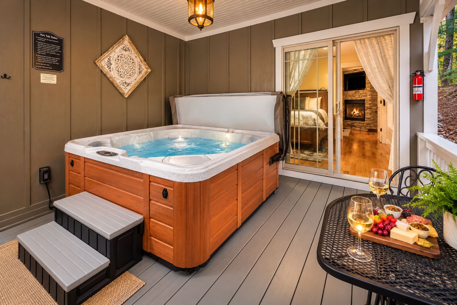Un bain à remous avec des marches et un coffret en bois, une table de patio avec une bouteille de vin et des fruits, et une cheminée en pierre.