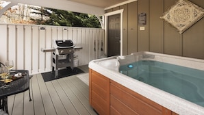 A hot tub on a wooden deck with a grill and a table set for dining. - Quiet, Family-Run Cottage Near Asheville (Asheville)