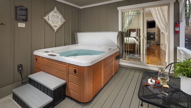 A hot tub with wooden steps, a patio table with wine glasses and fruit, and a stone fireplace. - Quiet, Family-Run Cottage Near Asheville (Asheville)