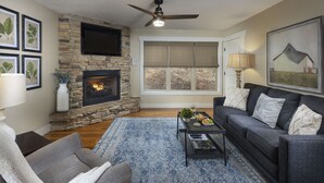 A living room with a stone fireplace, a gray sofa, a blue patterned rug, and a ceiling fan. - Quiet, Family-Run Cottage Near Asheville (Asheville)