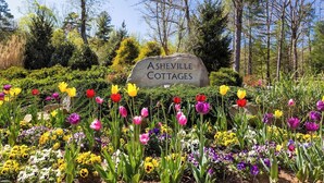 A sign for Ashville Cottages surrounded by a garden with various colorful flowers. - Quiet, Family-Run Cottage Near Asheville (Asheville)