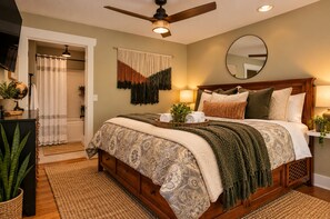 A bedroom with a bed, a ceiling fan, a mirror, and a bedside table with a lamp. - Quiet, Family-Run Cottage Near Asheville (Asheville)