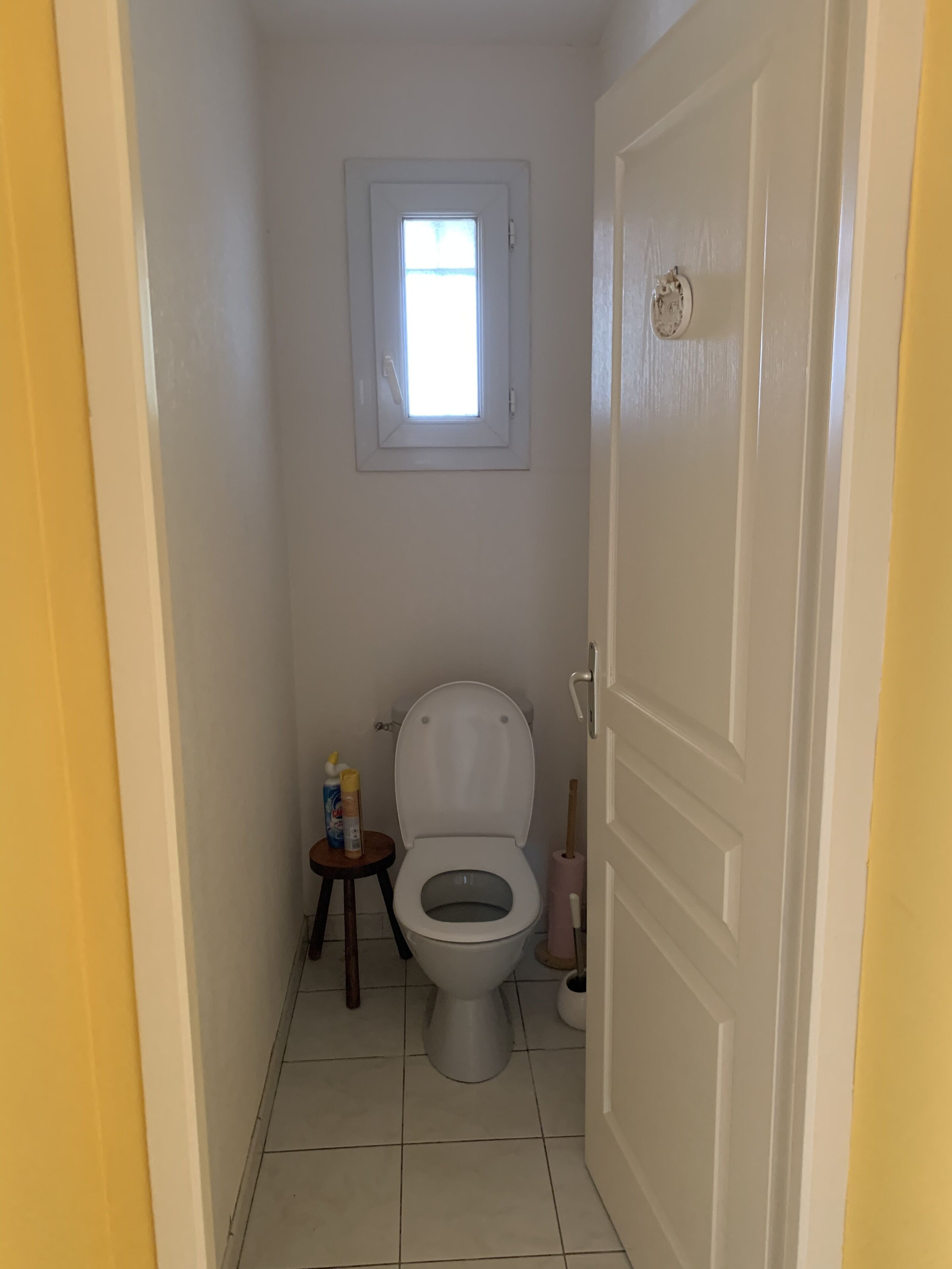 A small bathroom with a toilet, a window, and a door.
