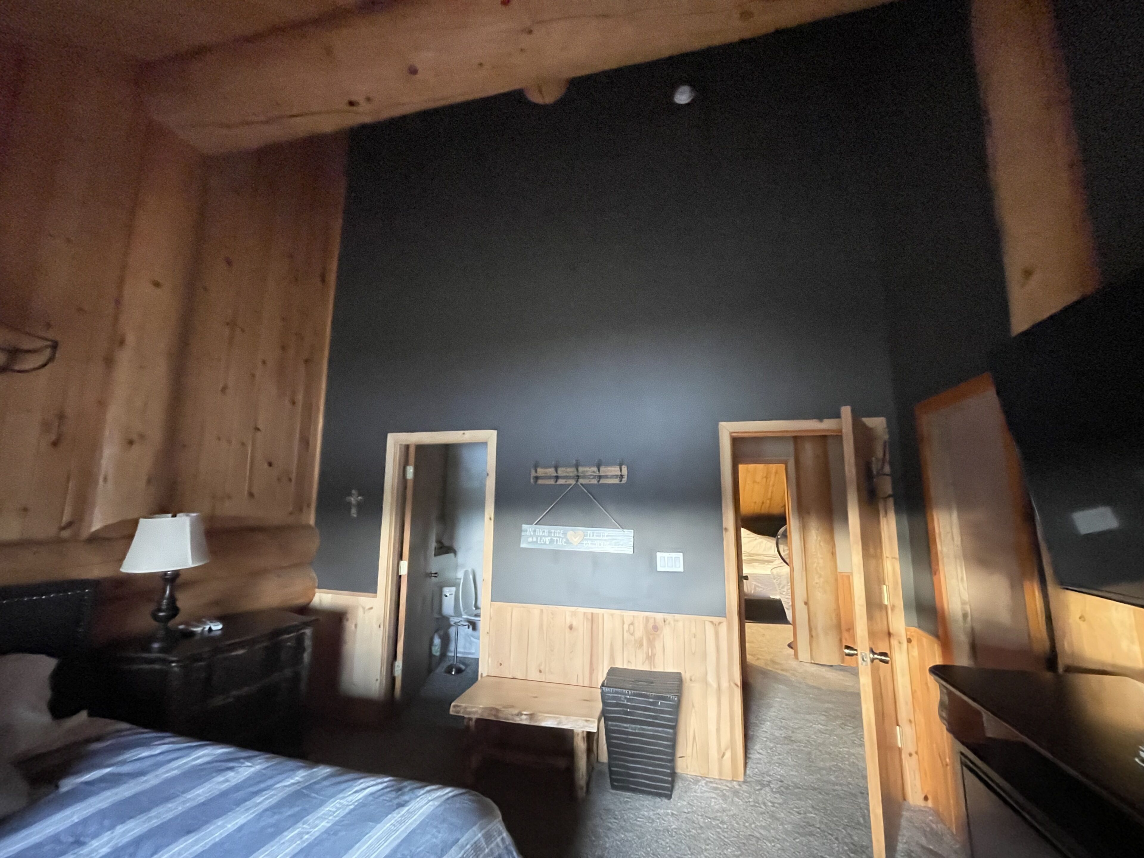Ett rum med en säng, ett skrivbord, en stol, ett litet bord och en tv. Det finns två dörrar som leder till andra rum.