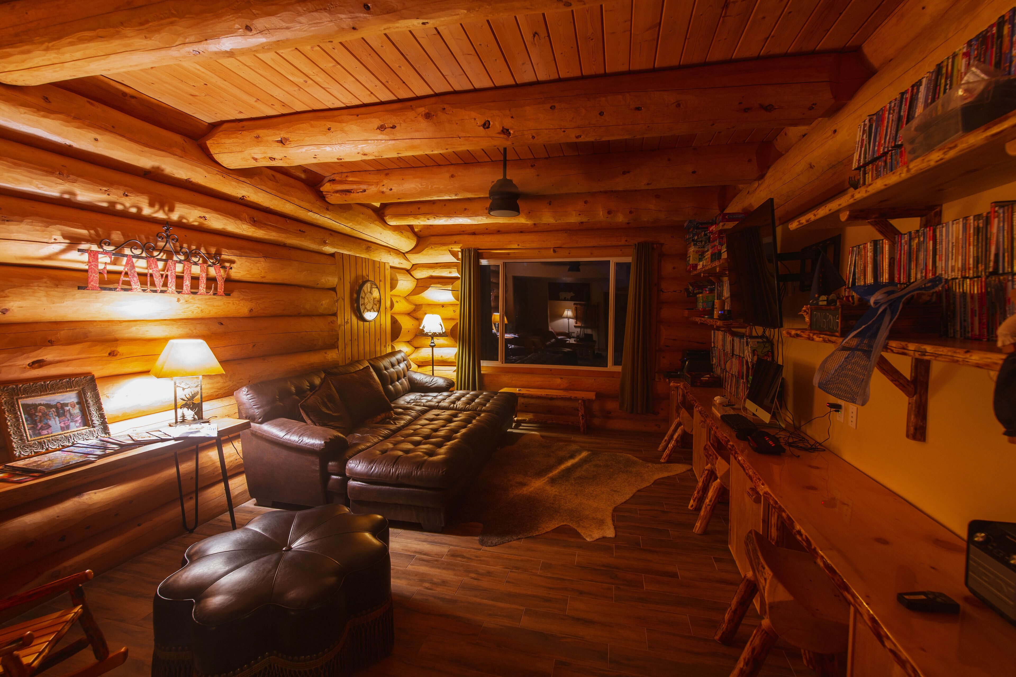 Interior acogedor de una cabaña de troncos con un sofá de cuero, un sillón mecedor de madera y una estantería llena de libros.
